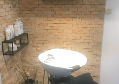 Untreated wall decoration in a corner in a hair dressing salon. Black shelves mounted on the wall and a chair in the front