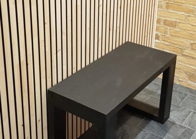 Wooden wall covering of slats with black painted grooves and a black bench