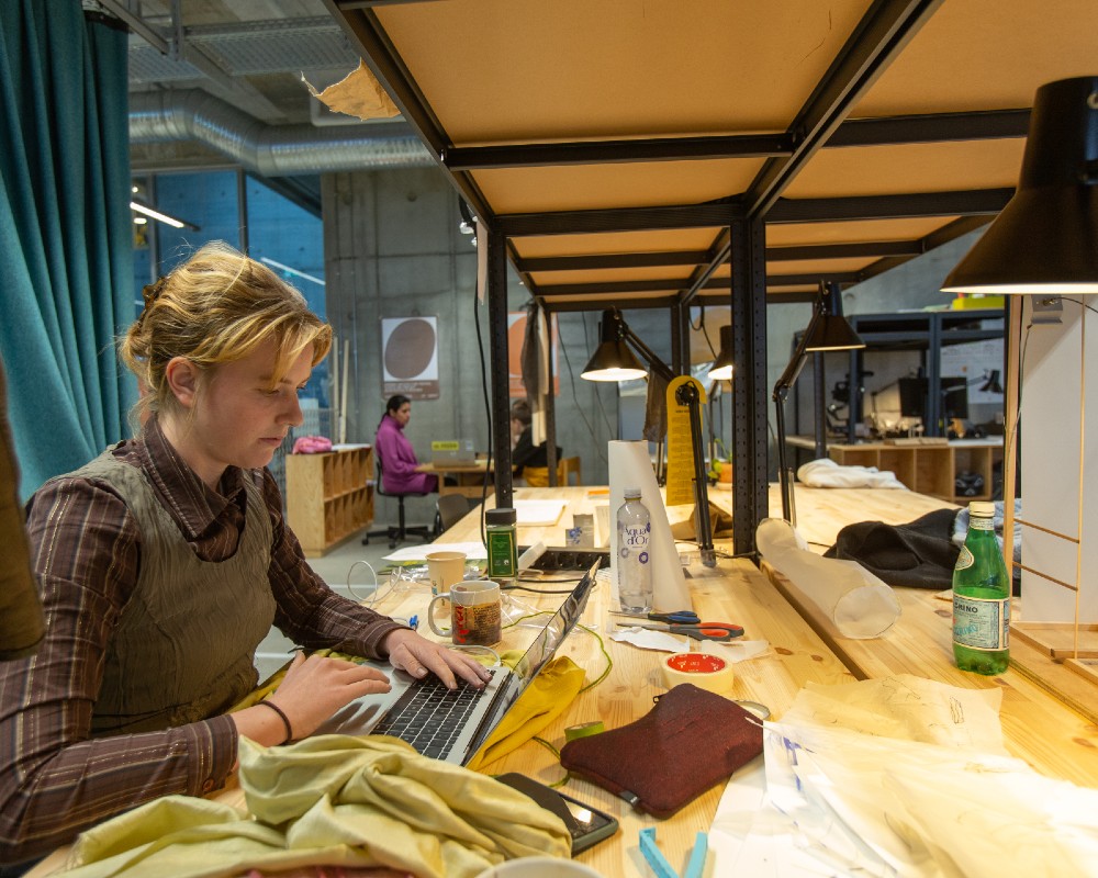 Studerende sidder ved skrivebordsplade i fyrretræ ved et tegnebord på Arkitektskolen Aarhus